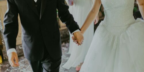 woman wearing white wedding gown holding hands with man while walking